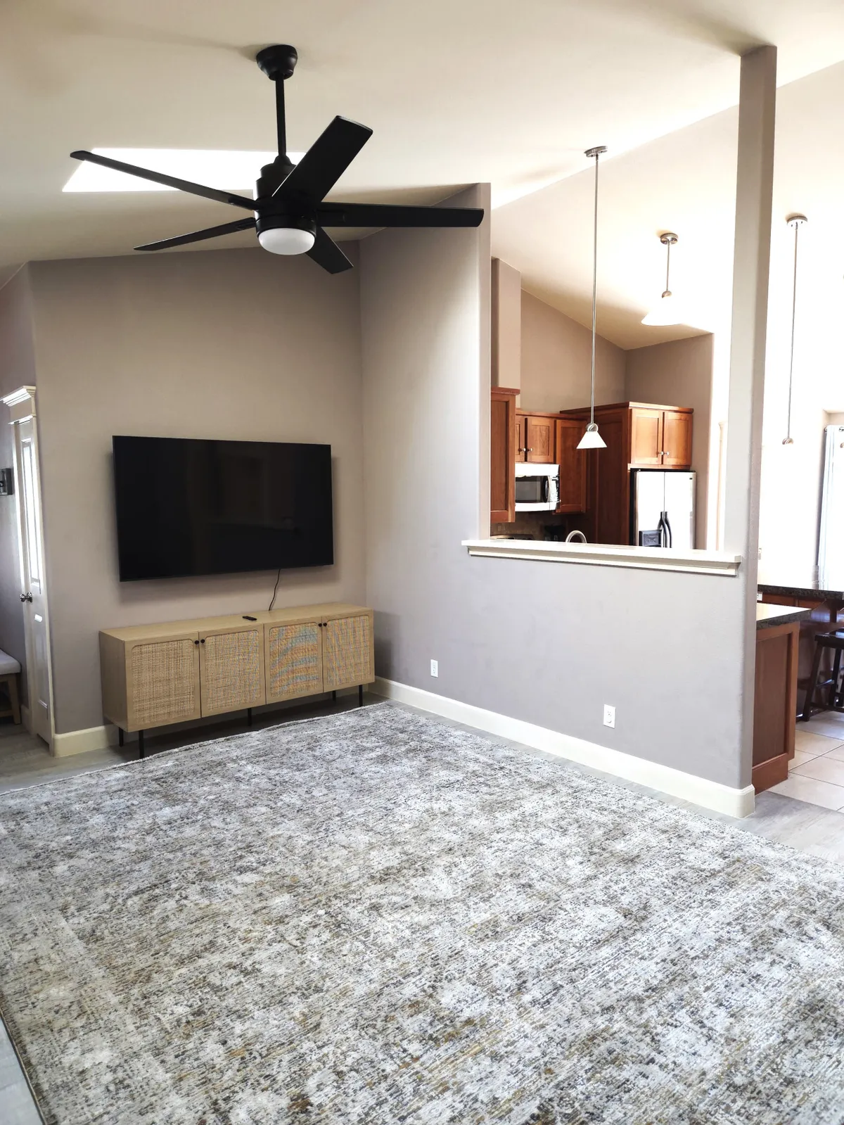 A cozy, modern living room with a ceiling fan, television, console cabinet, and a plush rug—an inviting space for relaxing or enjoying a movie night after a day in the snow.