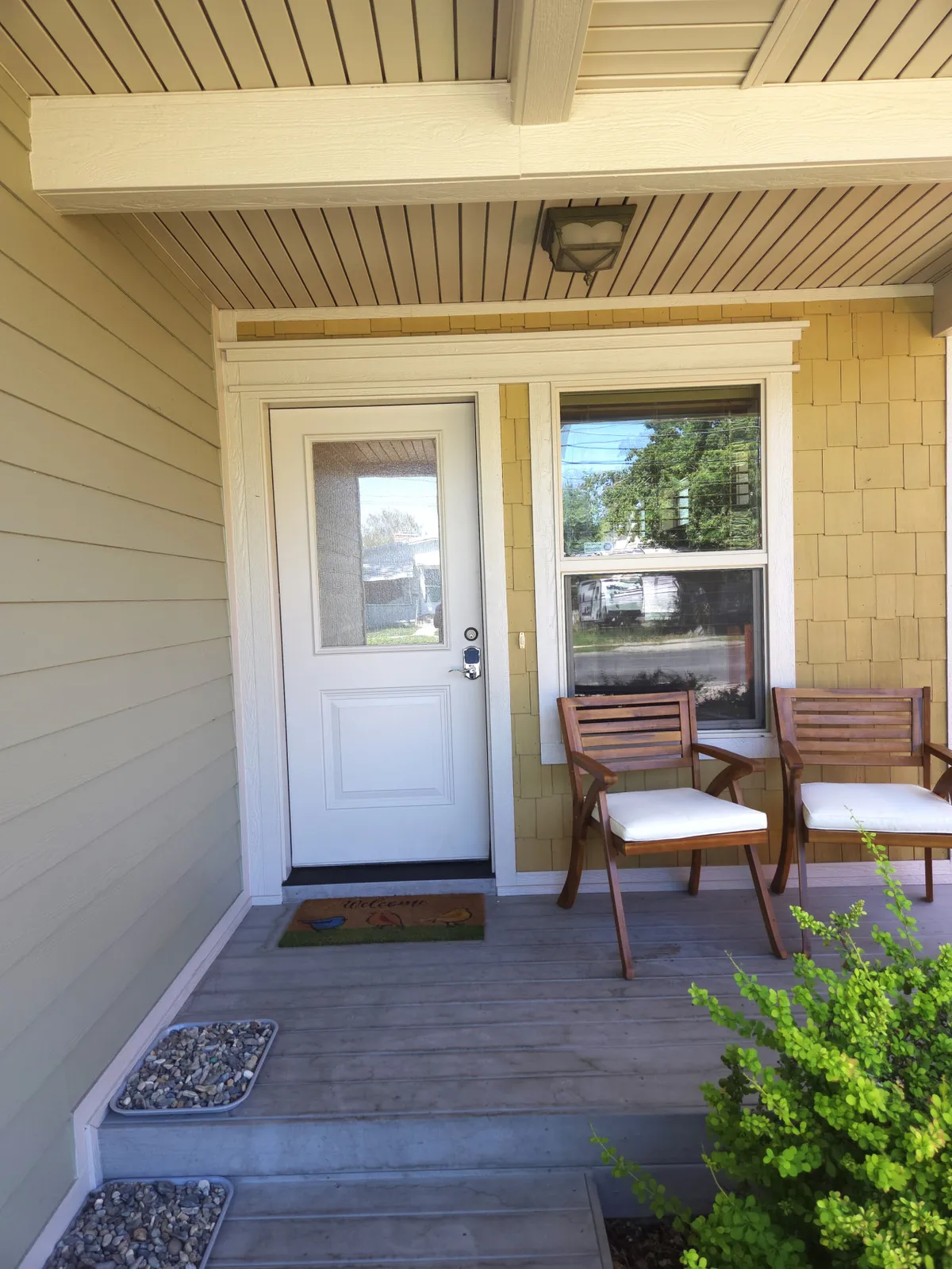 An exterior view of the front entryway, featuring a stylish door, wooden chairs, a welcome mat, and attractive landscaping. The setup conveys a sense of arrival and hospitality, suitable for welcoming guests back after a day on the green.