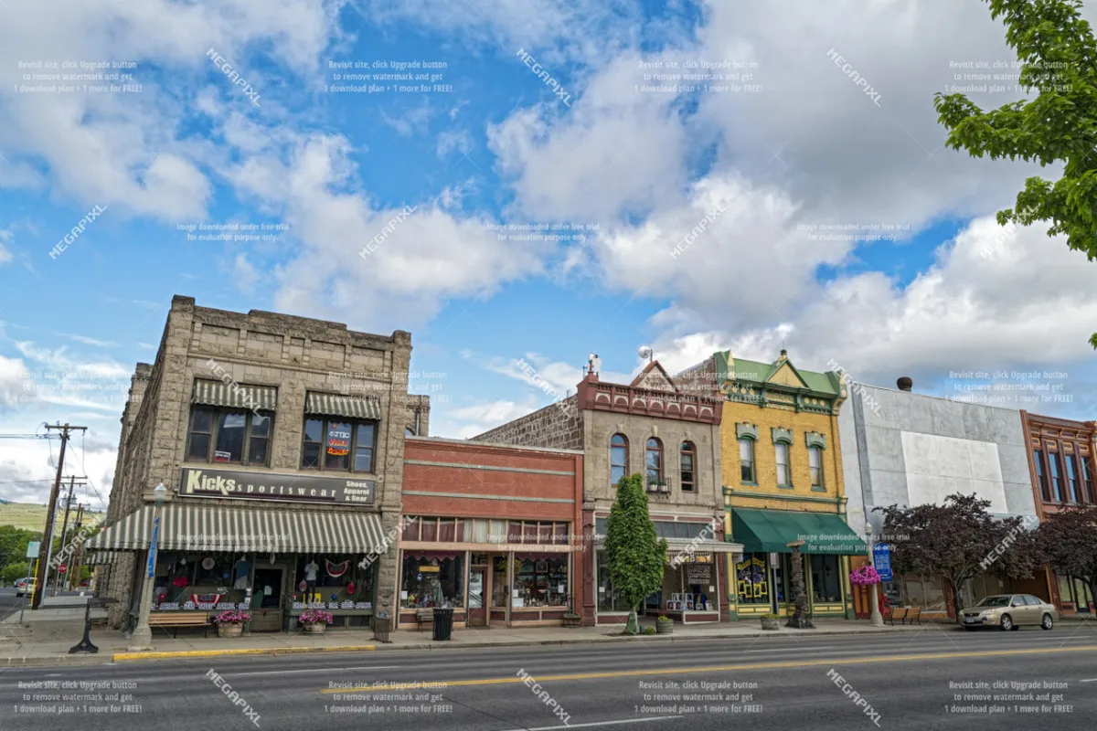A vibrant, colorful street scene showcasing the Kicks sportswear building surrounded by a variety of storefronts and tree-lined sidewalks. The atmosphere is lively with a welcoming small-town feel, ideal for strolling, shopping, or people-watching.