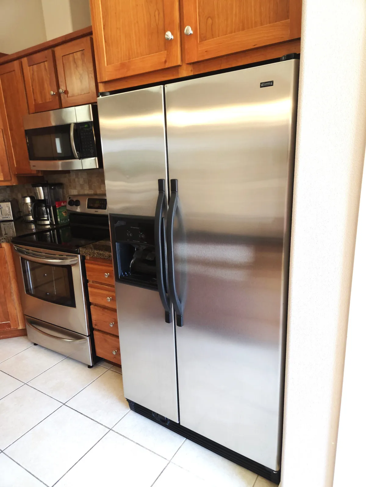 A modern kitchen with a stainless steel refrigerator, wooden cabinets, and various essential kitchen appliances. The layout is practical and family-friendly, emphasizing the space's capacity for meal preparation and social interaction.