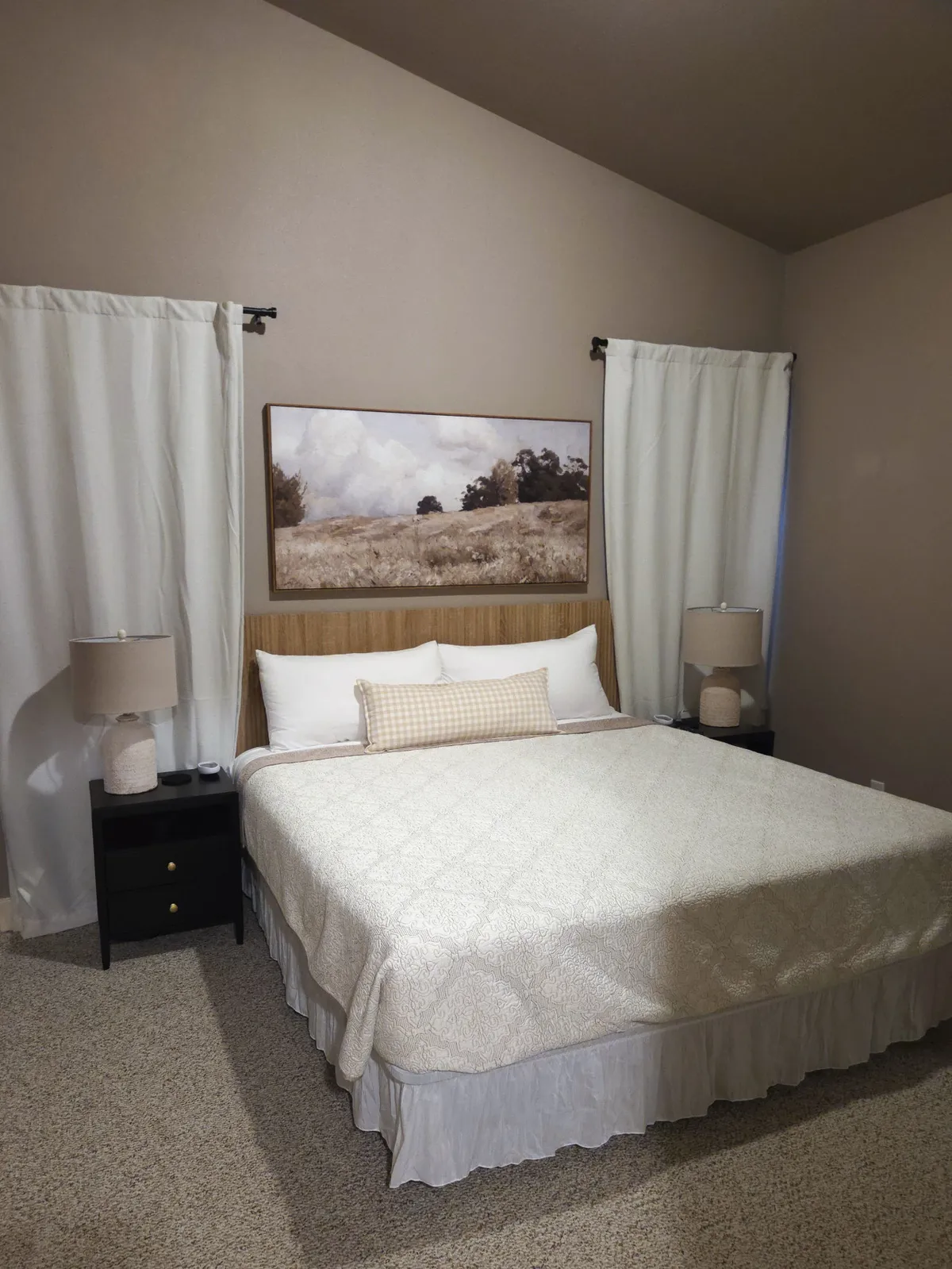 A tranquil bedroom with a large, inviting bed, artwork above the headboard, and nightstands topped with lamps on either side. The room exudes a cozy and serene ambiance, ideal for relaxation and restful nights.